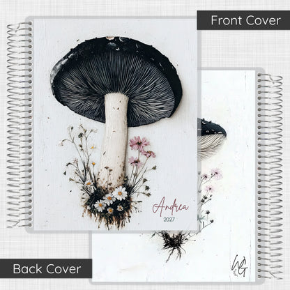 A spiral-bound notebook shown from both front and back covers. The front cover features a large black-and-white mushroom illustration with small pink and white flowers, and the name 'Andrea 2027' in script.