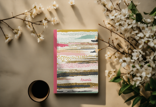 a colorful notebook with a floral design, a cup of coffee, and white flowers on a beige background.